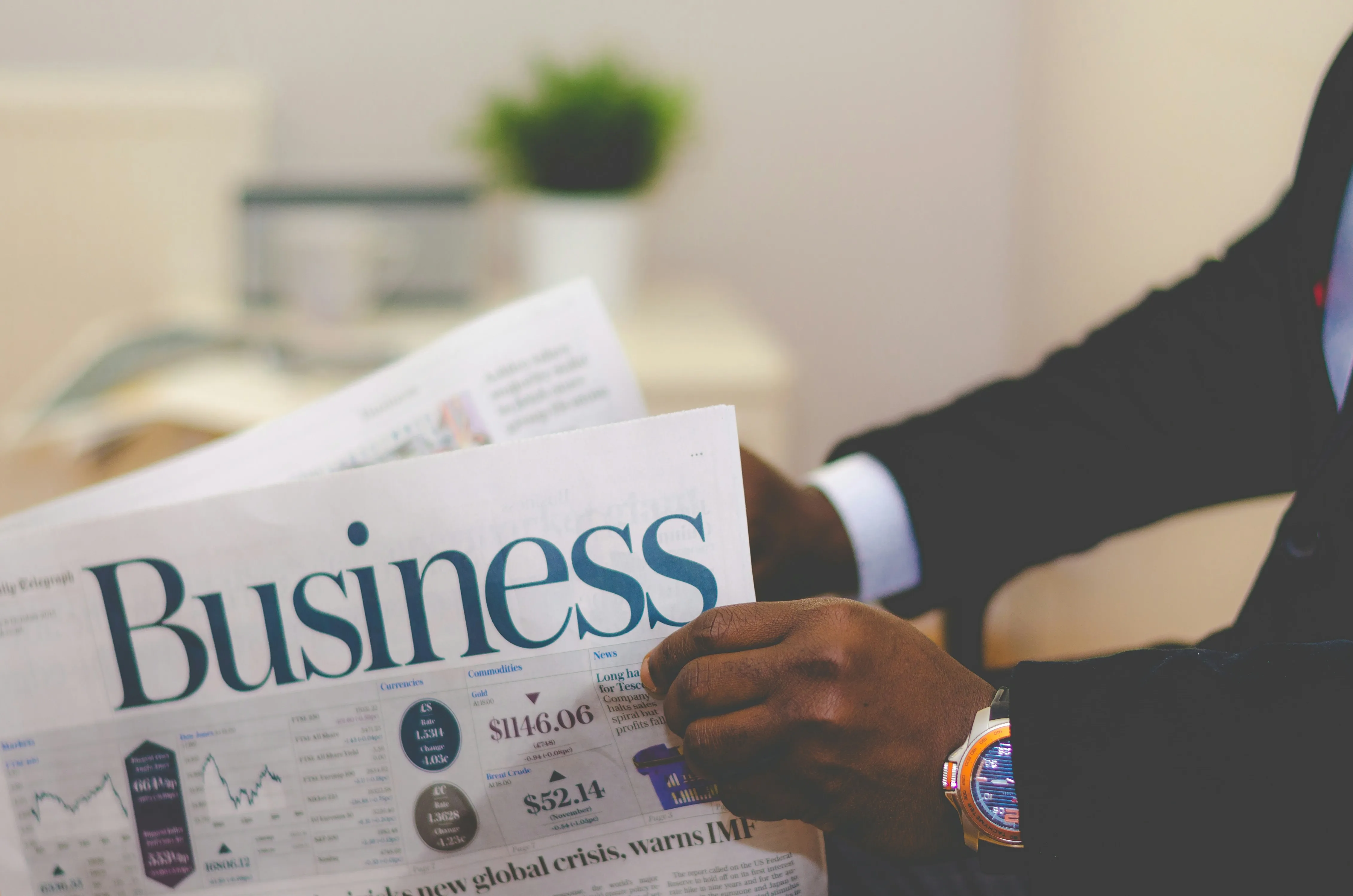 Person in suit reading a business newspaper with financial data and charts visible.