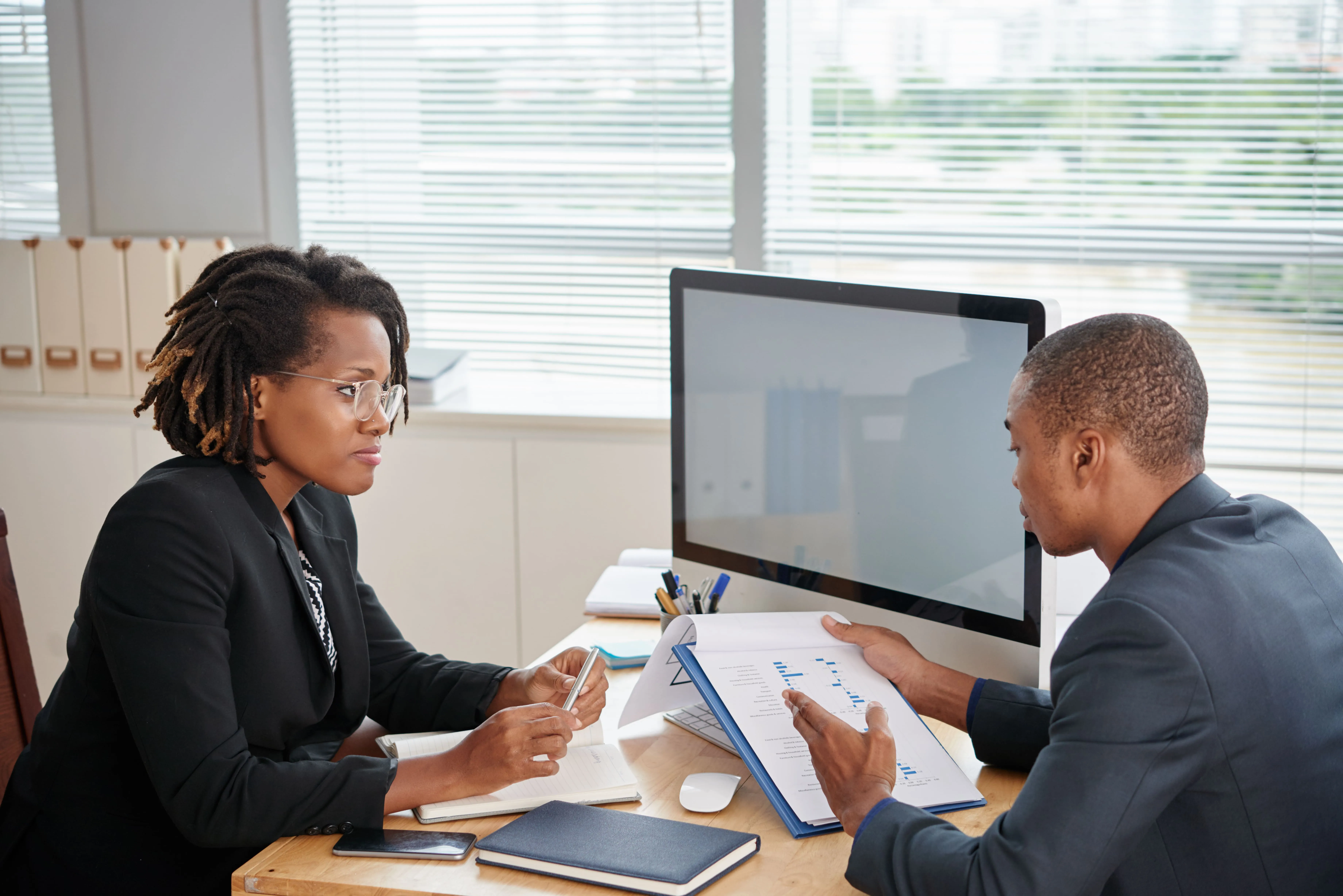Two business professionals discussing documents with charts in an office setting.
