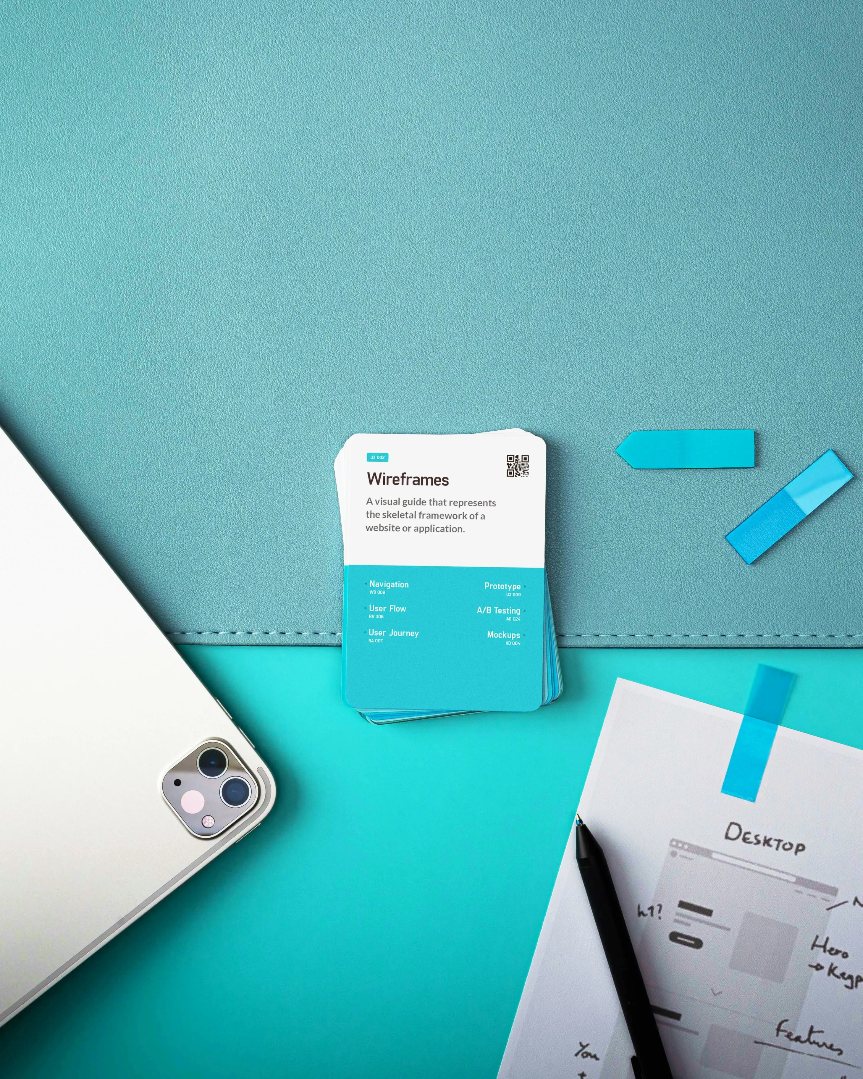 Top view of a tablet, wireframe cards, sticky notes, pen, and a sketched desktop wireframe on blue surface.