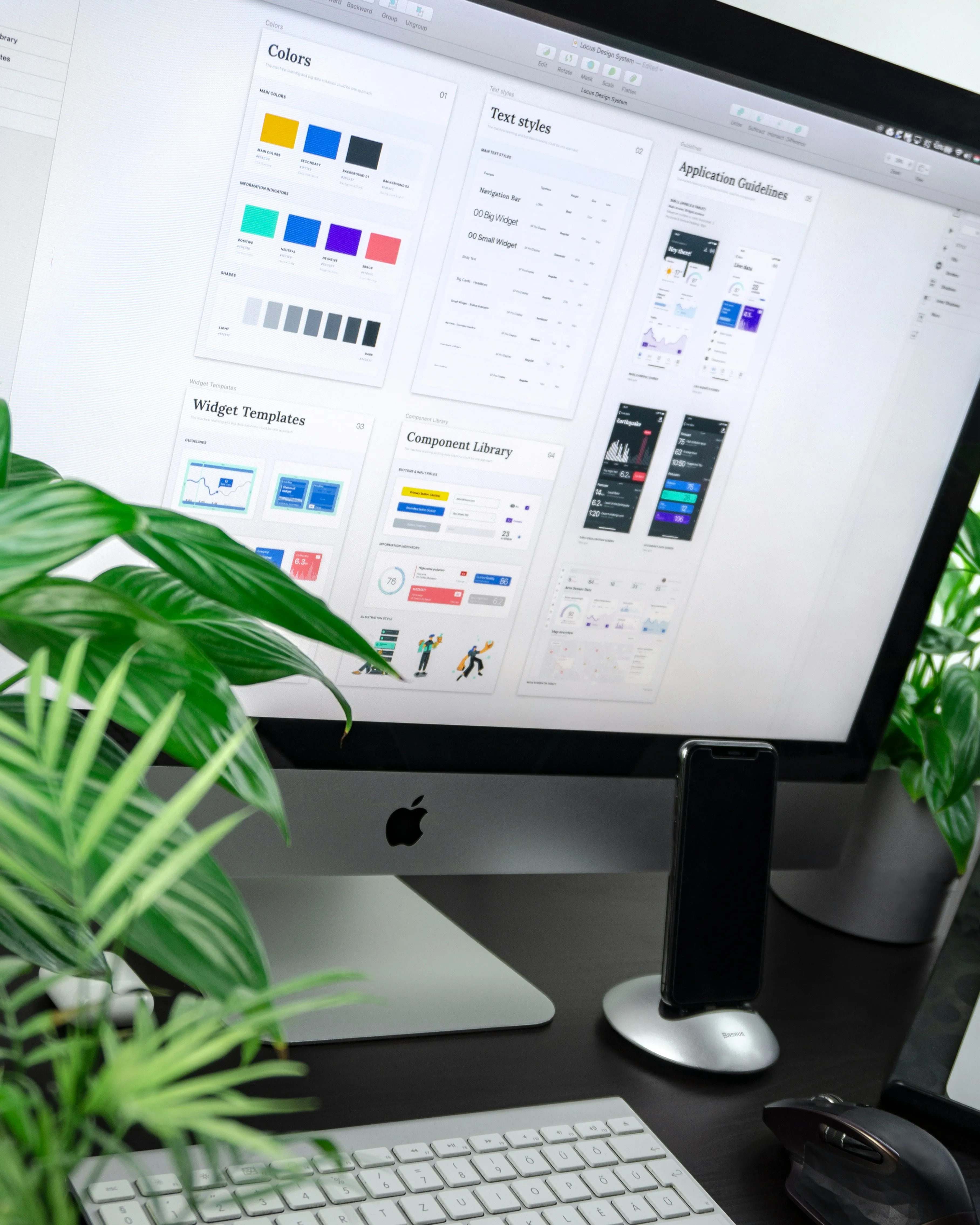 Desktop computer screen showing UI design templates with keyboard, mouse, phone, and plants on desk.