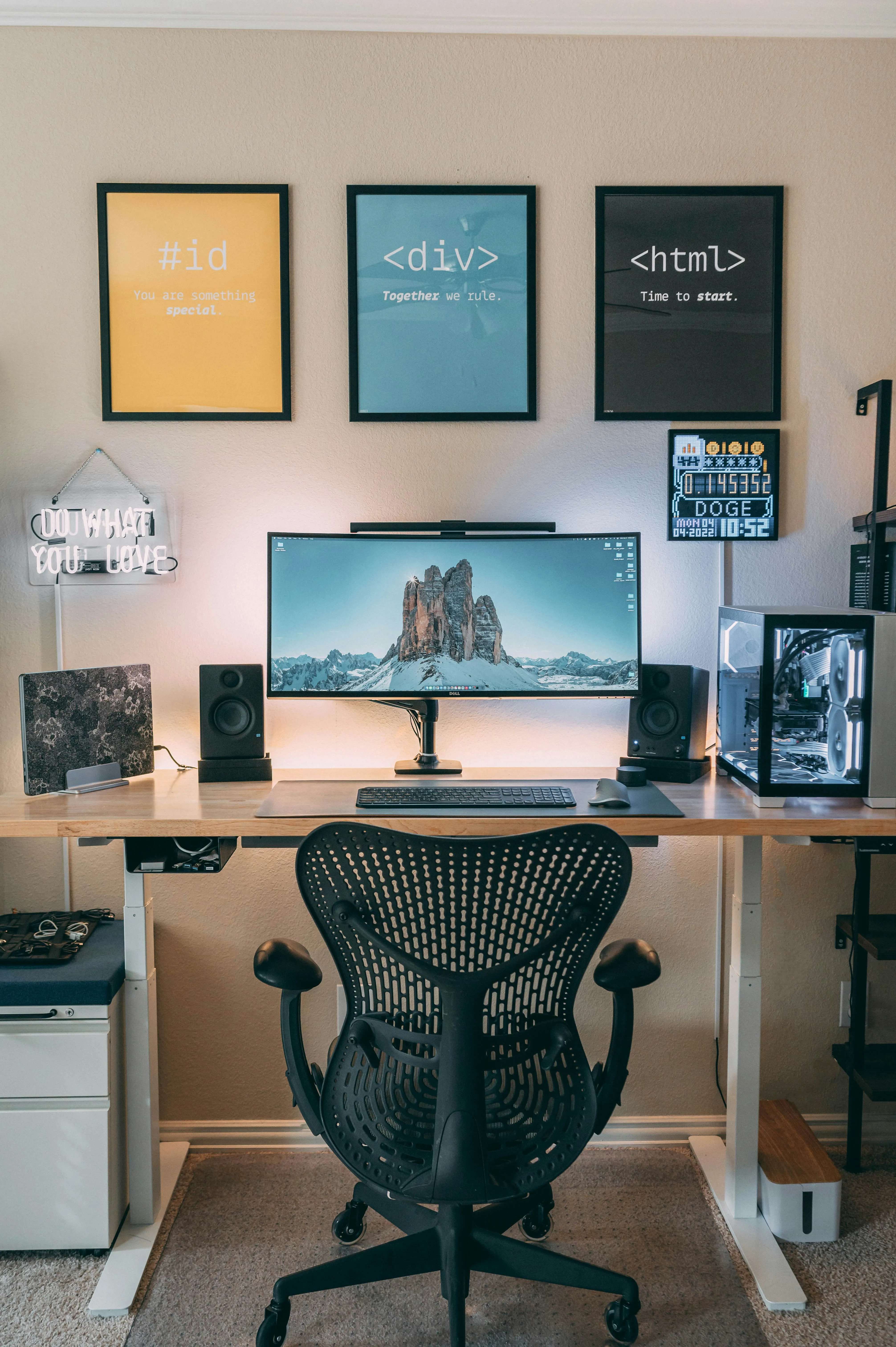 Modern desk setup with black chair, ultrawide monitor, speakers, PC tower, and three coding-themed posters.