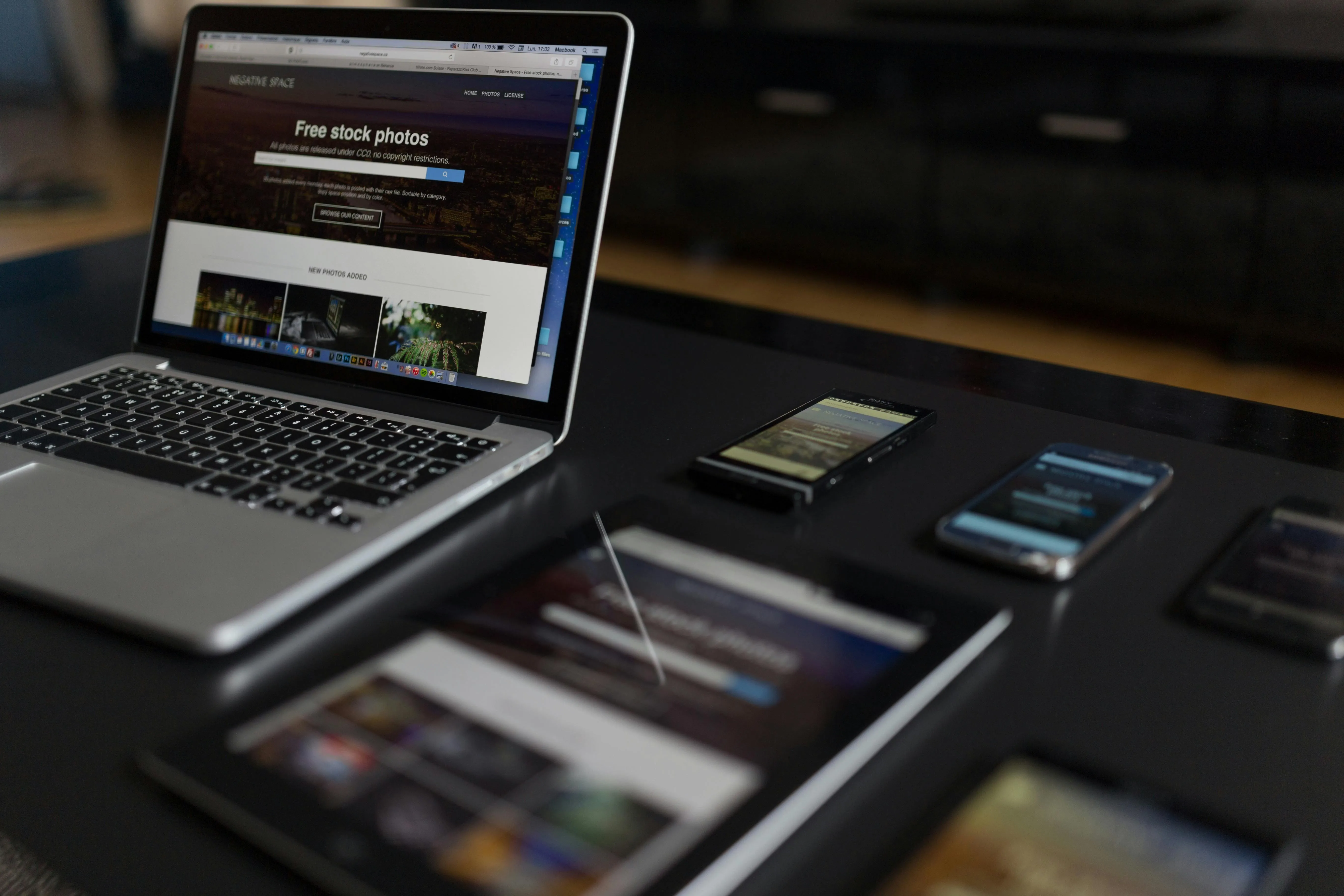 Laptop, tablet, and multiple smartphones on a black table displaying free stock photo website pages.