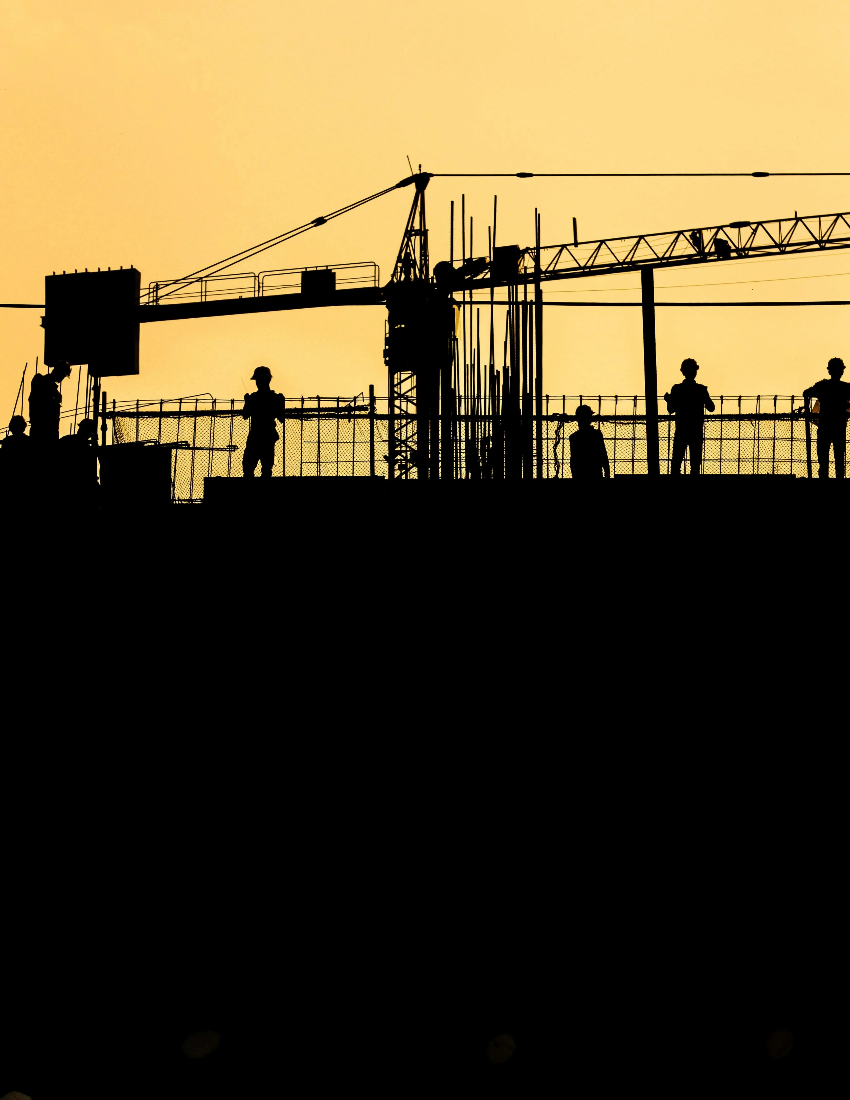 Silhouettes of five workers on a construction site with crane and metal framework at sunset.
